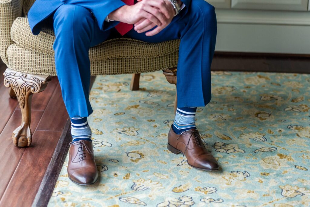 Uomo in abito blu seduto con calzini a righe e scarpe marroni